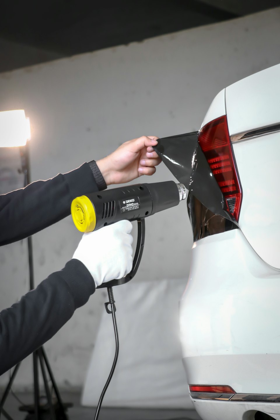 技術者が赤い車のテールランプにスモークフィルムを貼っています。